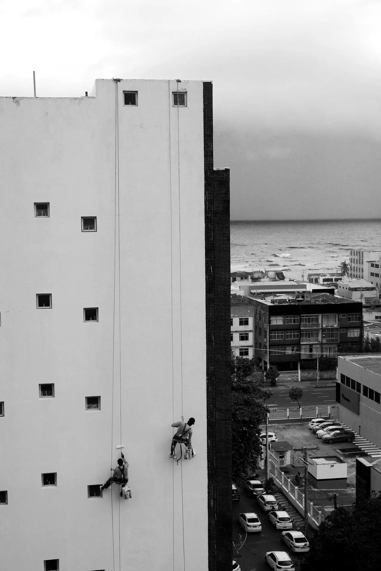 Workers rappel down a building facade near the ocean.